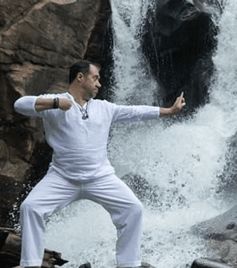 Jon Demel dressed in white, practicing a slow QiGong movement in front of a waterfall.