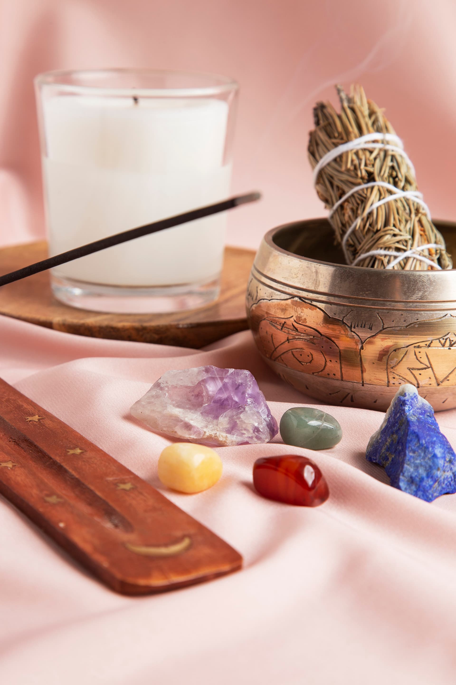 A singing bowl, candle and crystals arranged on a soft pink cloth.