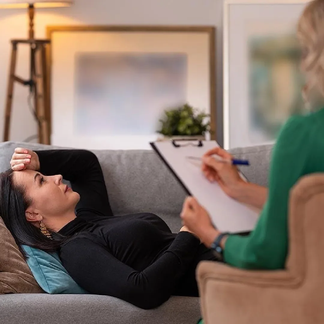 A client resting comfortably on a sofa while a practitioner listens and takes notes.